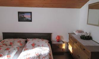 A cozy bedroom with two beds and floral bedding. A picture hangs on the wall, and there is a sideboard with a lamp and decorations.