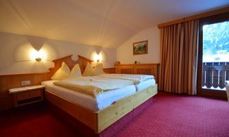 A cozy bedroom with a large bed and wooden details. The room has a warm atmosphere and a balcony with a view.