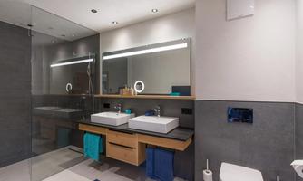 A modern bathroom with two sinks and large mirrors. The shower is separated by a glass wall and there are color-coordinated towels.