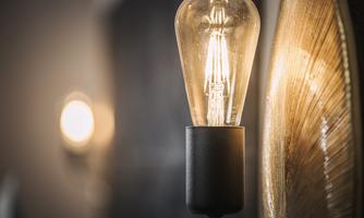 A stylish lamp with a light bulb gently illuminates. In the background, another light source is visible, creating a warm atmosphere.