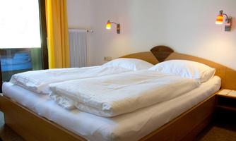 A cozy bedroom with a double bed and a window. The walls are painted in light colors, and there is soft lighting.
