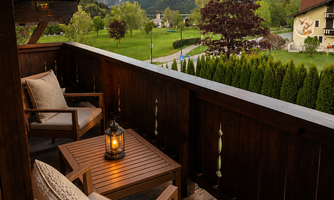 A beautiful balcony with wooden furniture and a lantern. In the background, mountains and a green landscape can be seen.
