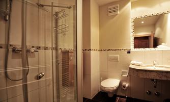 A modern bathroom with a shower cubicle, a marble sink, and a toilet. The walls are light tiled, and there is pleasant lighting.