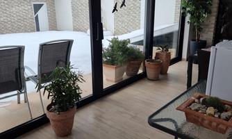A winter garden with large windows and a view of a snowy courtyard. In the room, there are plants and a table with pots.