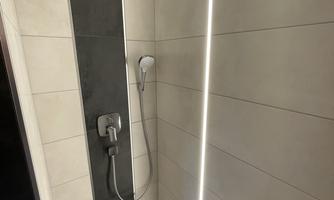 A modern shower with an elegant tiled wall and LED lighting. The showerhead is integrated into the ceiling.