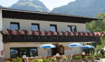 A charming restaurant with flowering balcony plants and outdoor umbrellas. In the background, the mountains are visible, creating a picturesque atmosphere.