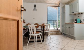 A bright kitchen with a table and chairs. Through the open door, there is a beautiful view of the mountains.