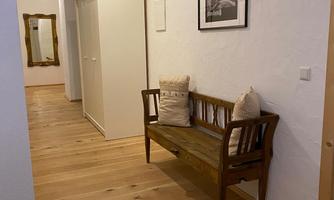 A bright hallway with wooden floors and a small wooden bench. A framed picture hangs on the wall and a mirror stands opposite.