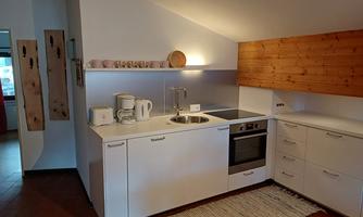 A modern kitchen with white cabinets and wood accents. It is well-equipped with a stove, a sink, and kitchen appliances.