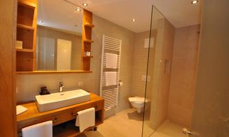 A modern bathroom with wooden shelves and a large sink. The glass shower cubicle and the bright tiles create an inviting atmosphere.