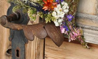 A rustic wooden sign with a heart-shaped flower arrangement. In the background, there is an old wooden door with an iron fitting.
