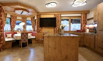 A modern kitchen with wooden surfaces and elegant furnishings. There is a dining table with cozy seating and large windows that let in plenty of light.