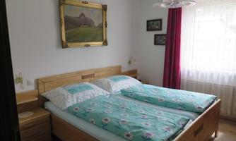 A cozy bedroom with a double bed and bright ceilings. Pictures hang on the walls, and in front of the window is a red curtain.
