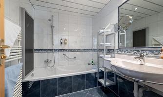 A modern bathroom with a bathtub and a shower. The walls are tiled in white and there is an elegant sink unit.