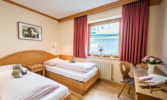 A cozy bedroom with two single beds and wooden decor. Soft colors and a window with a view outside create an inviting atmosphere.