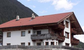 A traditional house in the mountains with a red tiled roof and wooden balustrades. The surroundings are green and mountainous, ideal for a peaceful retreat.