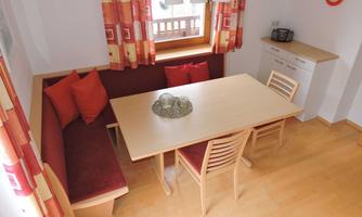 A cozy dining area with a large table and wooden chairs. The windows are adorned with colorful curtains and the walls are painted in light colors.