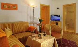 A cozy living room with a comfortable sofa and a table. In the background, there is a television and access to the bathroom.