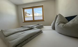 A bright bedroom with two beds and large windows. Outside, mountains can be seen and the room has a modern, cozy atmosphere.