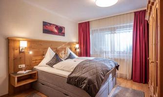 A cozy bedroom with a double bed and wooden paneling. Red curtains and warm light create an inviting atmosphere.