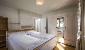 A cozy bedroom with aLarge bed and bright walls. In the background, there is a wardrobe and a window with a view outside.
