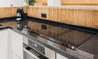 A modern kitchen with a smooth cooking surface made of black granite. The wood paneling and plants create a warm atmosphere.