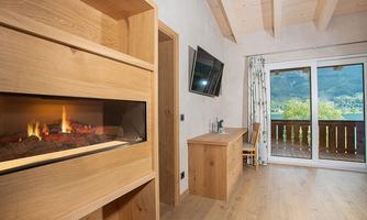 A cozy room with a modern wooden fireplace. Large windows offer a view of the surrounding nature.