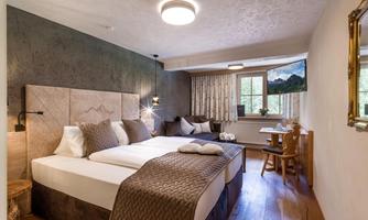 A modern bedroom with two beds, cozy decoration, and wooden flooring. Large windows offer a view of nature.