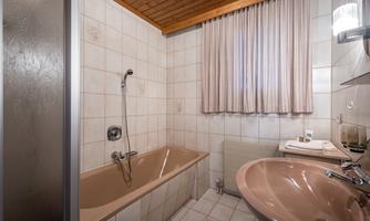 A bathroom with a bathtub and a sink. It has bright tiles and a wooden ceiling.