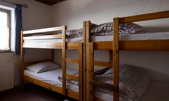 A simple room with two wooden bunk beds. The beds are unmade and there is a window with a blue curtain.