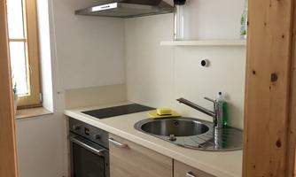 A modern kitchen with wooden shelves and a stove. The walls are light, and there is a window that lets in light.