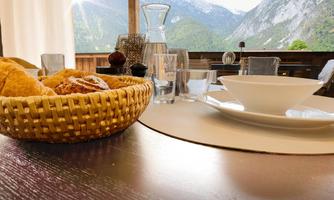 A table with a basket full of rolls and a white plate. In the background, the mountains and nature are visible.
