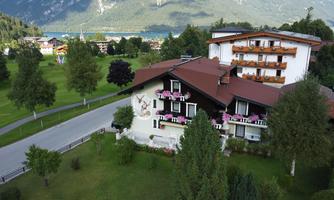 A charming house with balcony flowers in a green landscape. In the background, there are mountains and a clear lake.