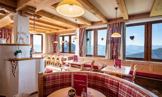 A cozy restaurant with a wooden ceiling and large windows. The decor is rustic with red and white colors, and there is a beautiful view of the mountains.
