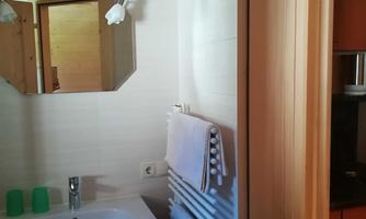 A modern bathroom with a sink, a mirror, and towels. The walls are light and made of wood, creating a cozy atmosphere.