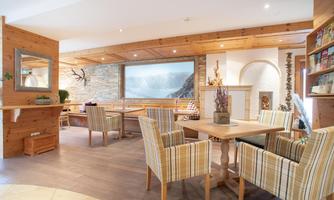A cozy interior with wooden furniture and comfortable armchairs. In the background is a large window with a beautiful view of nature.