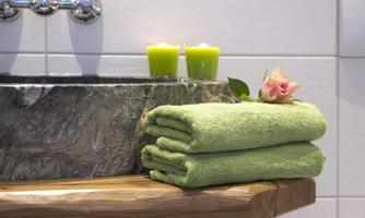 A quiet bathroom area with stacked green towels. Two green candles and a flower enhance the relaxing atmosphere.