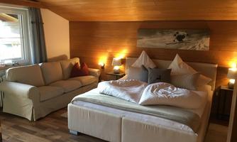 A cozy bedroom with a large bed and a modern couch. Warm light creates an inviting atmosphere.