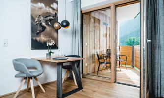 A modern room with a small table and chairs. A large window front leads to a balcony overlooking nature.