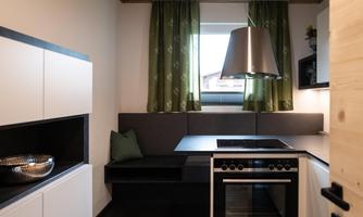 A modern kitchen with elegant black and white cabinets. Green curtains and a cozy seating area give the room an inviting atmosphere.