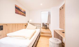 A modern room with a single bed and a minimalist design. The light hardwood floor and the artwork on the wall create a friendly atmosphere.