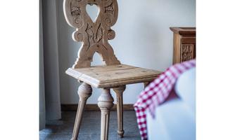 A beautiful wooden chair with an intricately carved back. The chair has four stylish legs and stands in a bright room.