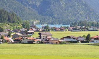 A picturesque landscape with green meadows and traditional houses. In the background, a clear lake and mountains can be seen.