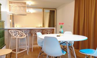 A modern dining room with a round table and bright chairs. In the background, there is a bar with seating and decorative elements.