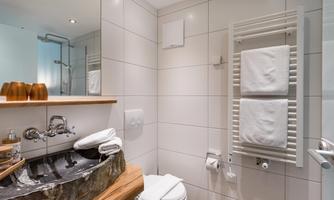 A modern bathroom with a natural stone sink and a wooden shelf. Towels are neatly arranged on a towel rack.