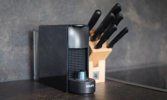 A modern kitchen slicer from Krups stands on a countertop. Next to it is a wooden block with several kitchen knives.