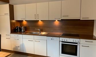 A modern kitchen with white cabinets and wooden accents. It is well equipped with a stove, oven, and sink.