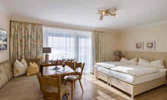 A bright and cozy hotel room with a double bed and a dining area. Large windows let in plenty of light and create a pleasant atmosphere.