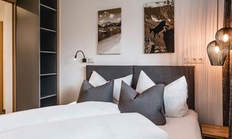 A modern bedroom with a cozy double bed and elegant pillows. Two pictures with landscape motifs hang on the wall, and a stylish lamp provides pleasant light.