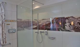 A modernly designed bathroom with a glass shower. On the wall, there is a mountainous landscape picture.